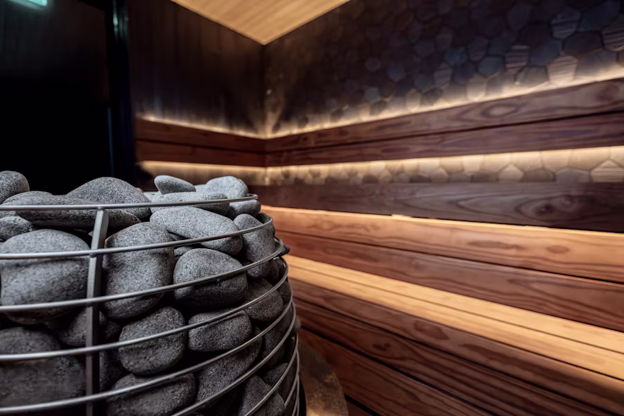 Close-up of smooth sauna stones inside a modern wooden sauna with warm lighting and natural wood paneling, creating a peaceful and relaxing atmosphere.