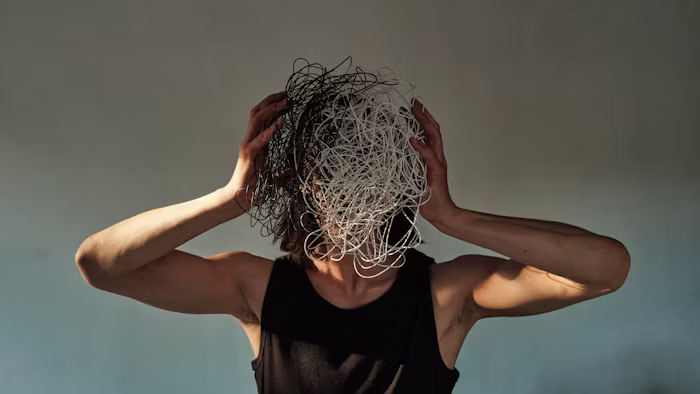 Person holding their head with tangled black and white wires covering their face, symbolizing climate anxiety, overwhelming stress, and the benefits of anxiety therapy, counseling, and treatment.